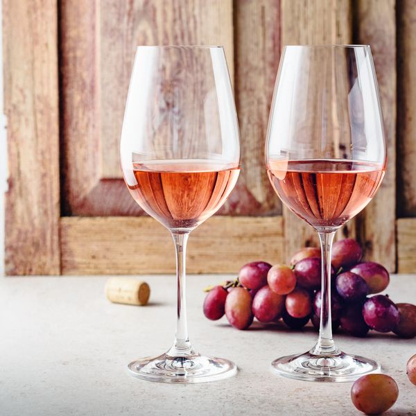 Two glasses of rosé wine with grapes and cork on table.
