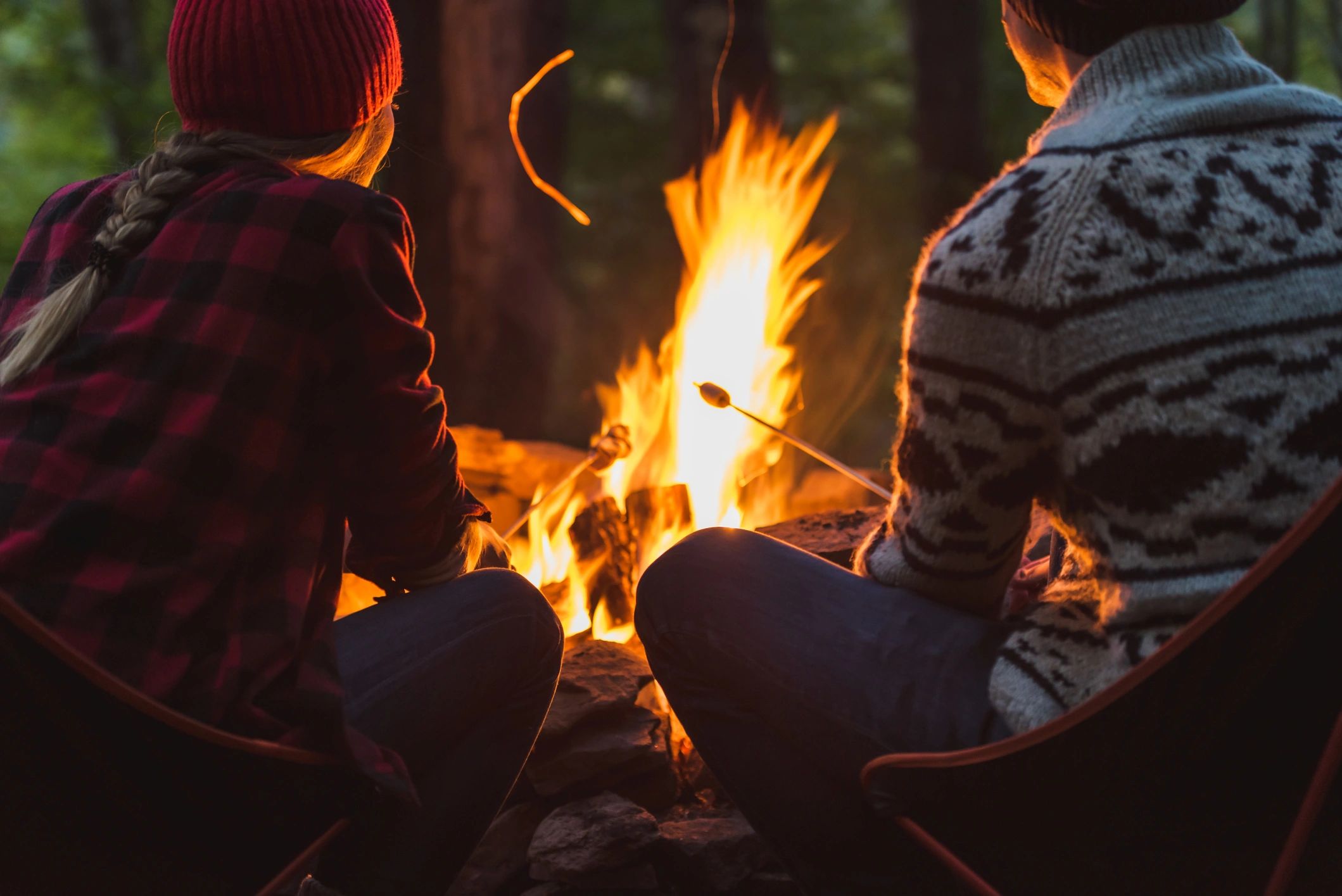 Two people roasting marshmallows by a campfire in cozy sweaters.
