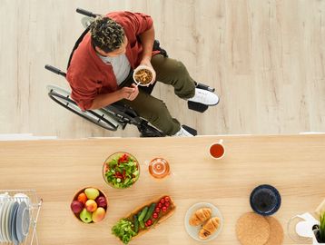 Person in wheelchair eating at kitchen counter.