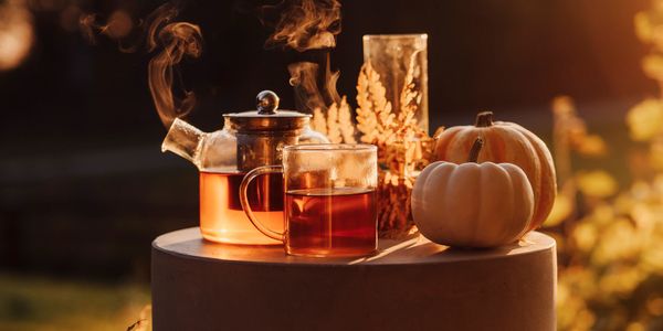 Steaming tea in glassware with pumpkins and autumn leaves at sunset.