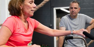 A woman exercises on a bike while a man watches attentively.