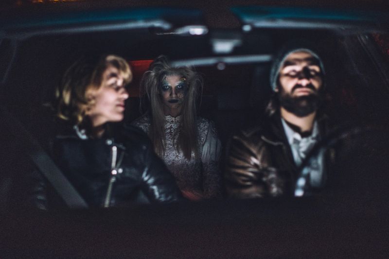 Young couple sitting in car with a scary witch/ghost/demon/monster/zombie behind them