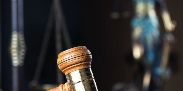 Wooden gavel with scales of justice and Lady Justice statue in background.