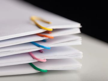 Stack of paper documents clipped with colorful paperclips.
