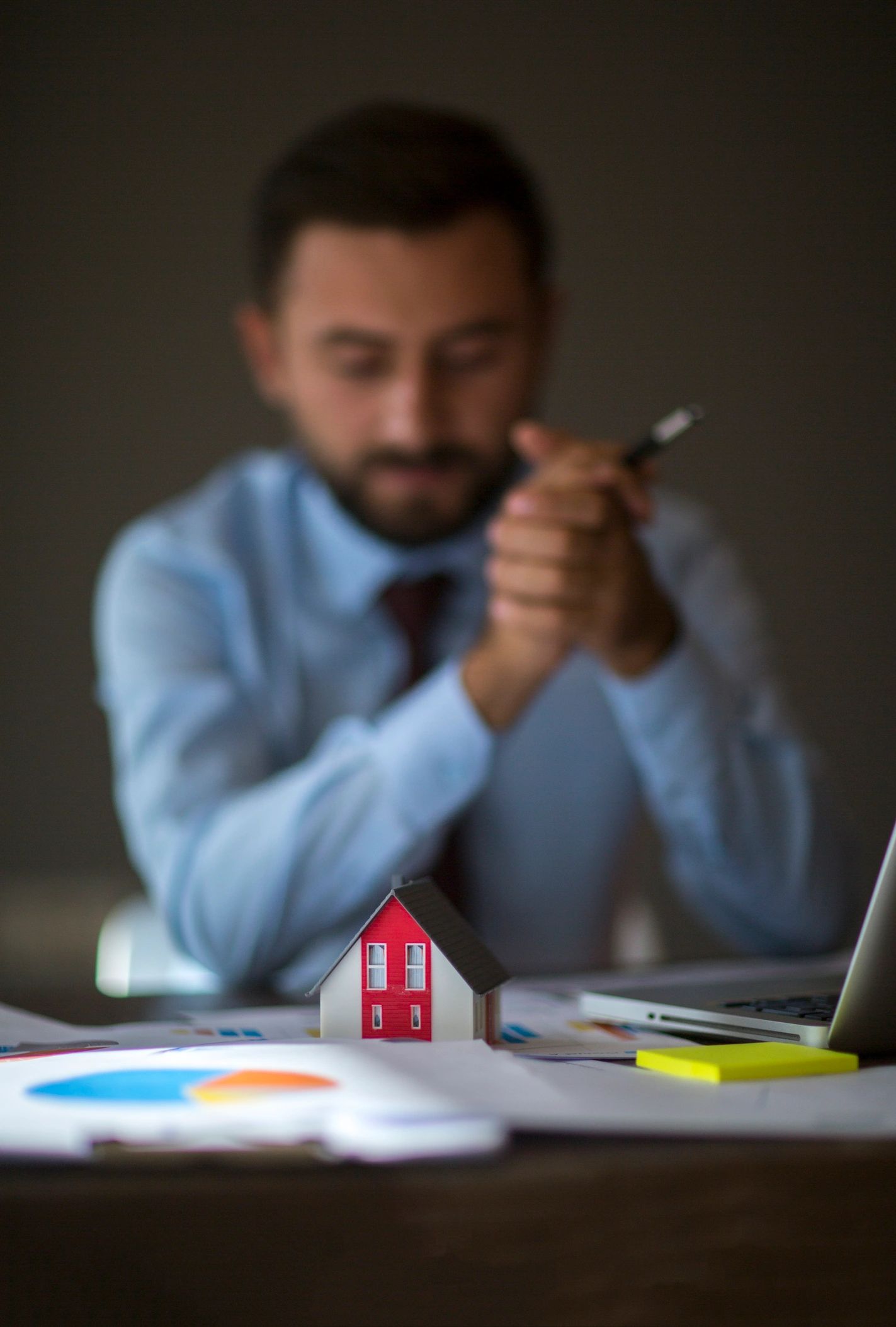Businessman contemplating a miniature house model on his desk.