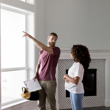 A man points outside a window while a pregnant woman listens attentively.