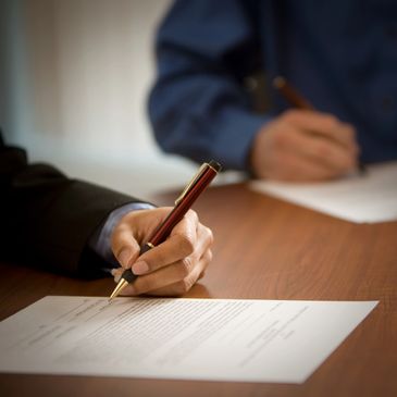 Two individuals signing documents at a wooden table.