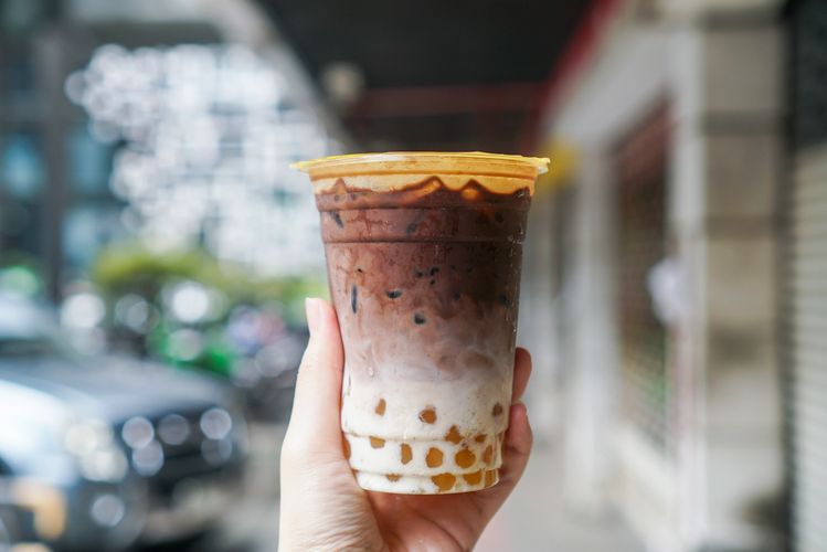 Hand holding a cup of iced chocolate milk tea with tapioca pearls.