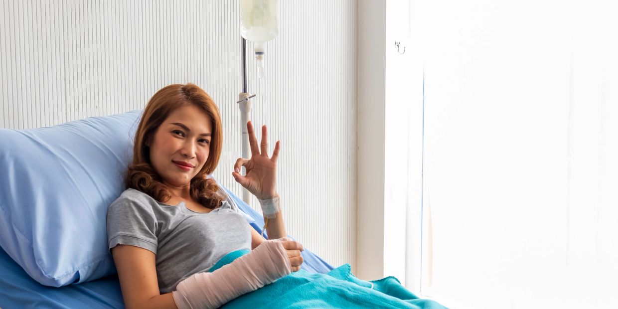 Woman in hospital bed showing okay sign.