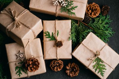 Rustic brown paper gifts decorated with pinecones and greenery on black surface.
