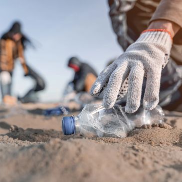 Hand with glove picking up plastic bottle on sandy beach during cleanup.