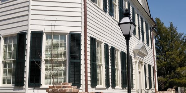 White colonial-style house with black shutters and a street lamp on a sunny day.