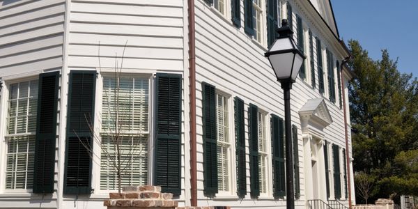 White colonial-style house with black shutters and a street lamp on a sunny day.