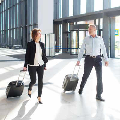 Two business travelers walking through an airport with rolling suitcases.