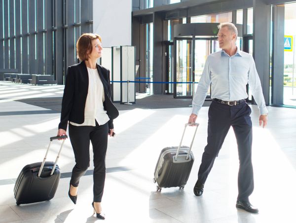 Two business travelers walking with suitcases in a modern airport terminal.