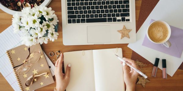 Desk with a laptop, notebook, flowers, and coffee.
