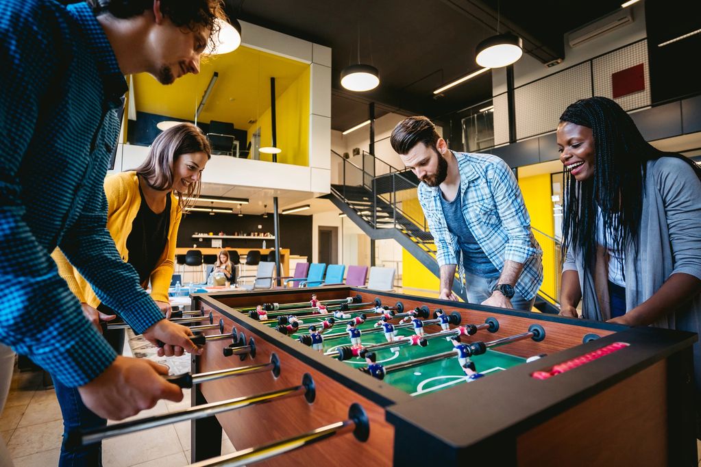 Four young adults enjoying a competitive foosball game in a modern office lounge.