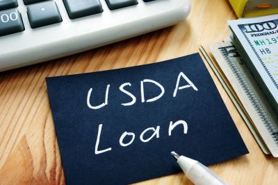 Note card with "USDA Loan" text, pen, money, and calculator on a wooden table.