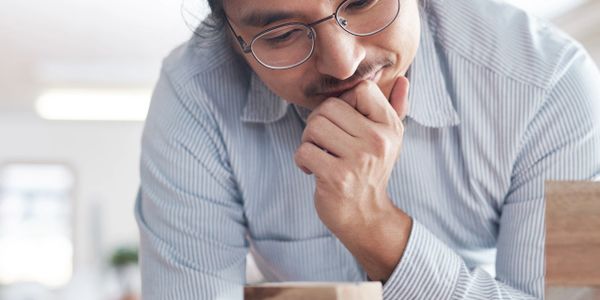 Man thoughtfully examining wooden blocks on a table.