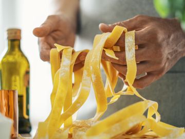 Hands holding fresh pasta ribbons with a bottle of olive oil nearby.