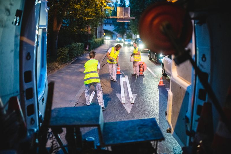 View from inside utility van of road painting crew giving arrow marking on Central European urban street a fresh coat of spray paint.