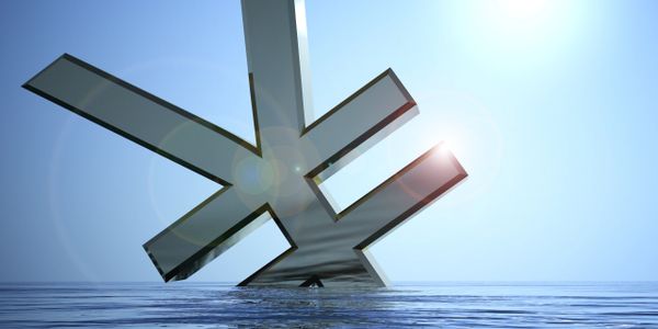 A large metallic yen symbol partially submerged in calm water under a bright sky.