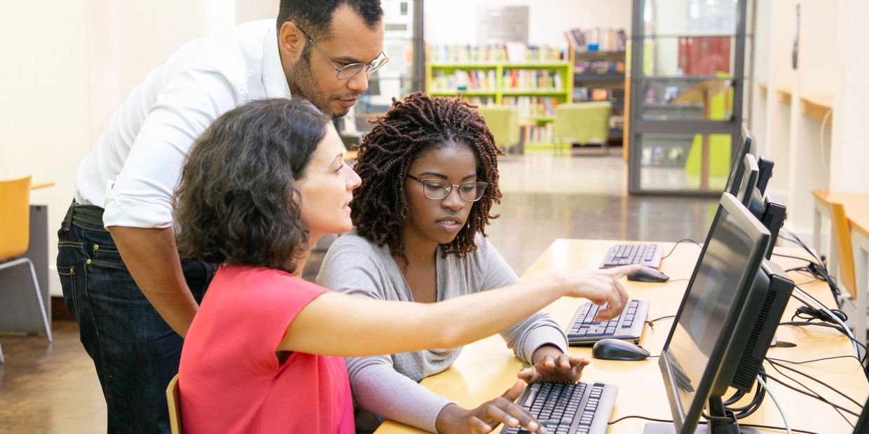 Three people collaborate on a computer in a bright office space.