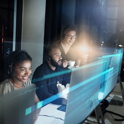 Three coworkers collaborating late at night with code on their screens.