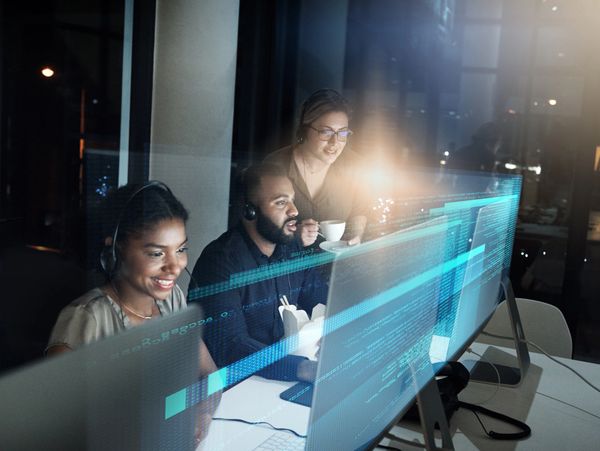 Three coworkers collaborating late at night with code on their screens.