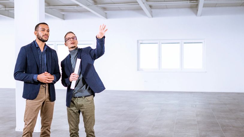 Two men in business attire discussing plans in an empty room.