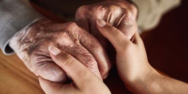 Young hands gently holding elderly hands, symbolizing care and compassion.