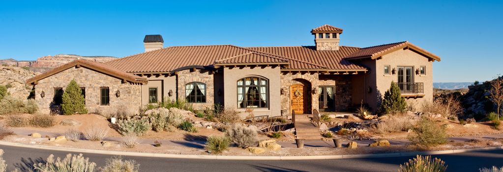 Large stone and stucco house with a tiled roof in a desert landscape.