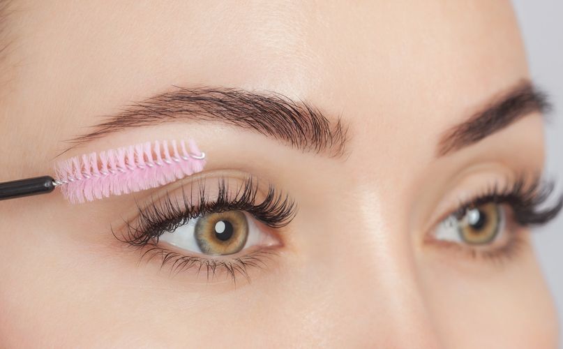 Close-up of a person grooming eyebrows with a pink spoolie brush.