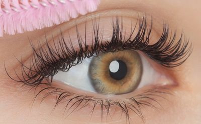 Close-up of a hazel eye with long eyelashes and a pink flower.