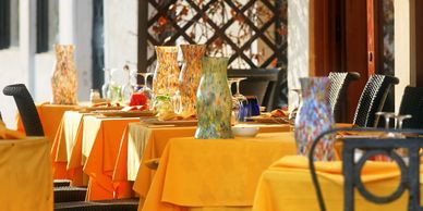 Outdoor dining area with yellow tablecloths and decorative vases on each table.