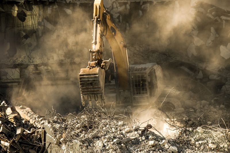 Machinery demolishing building and cleaning rubble