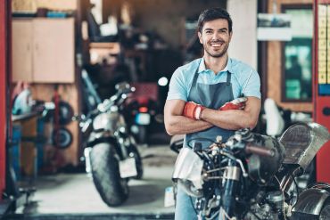 Man in an apron smiling in a motorcycle workshop.