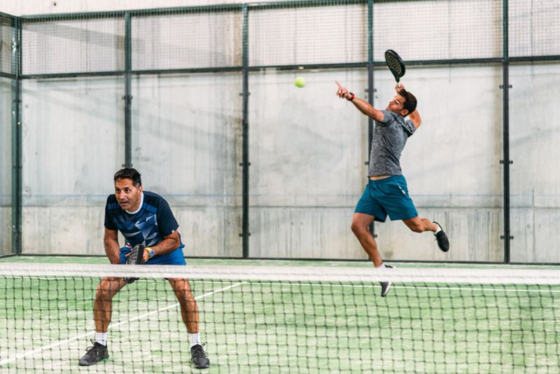 two padel player playing padel in a green grass padel court indoor behind the net