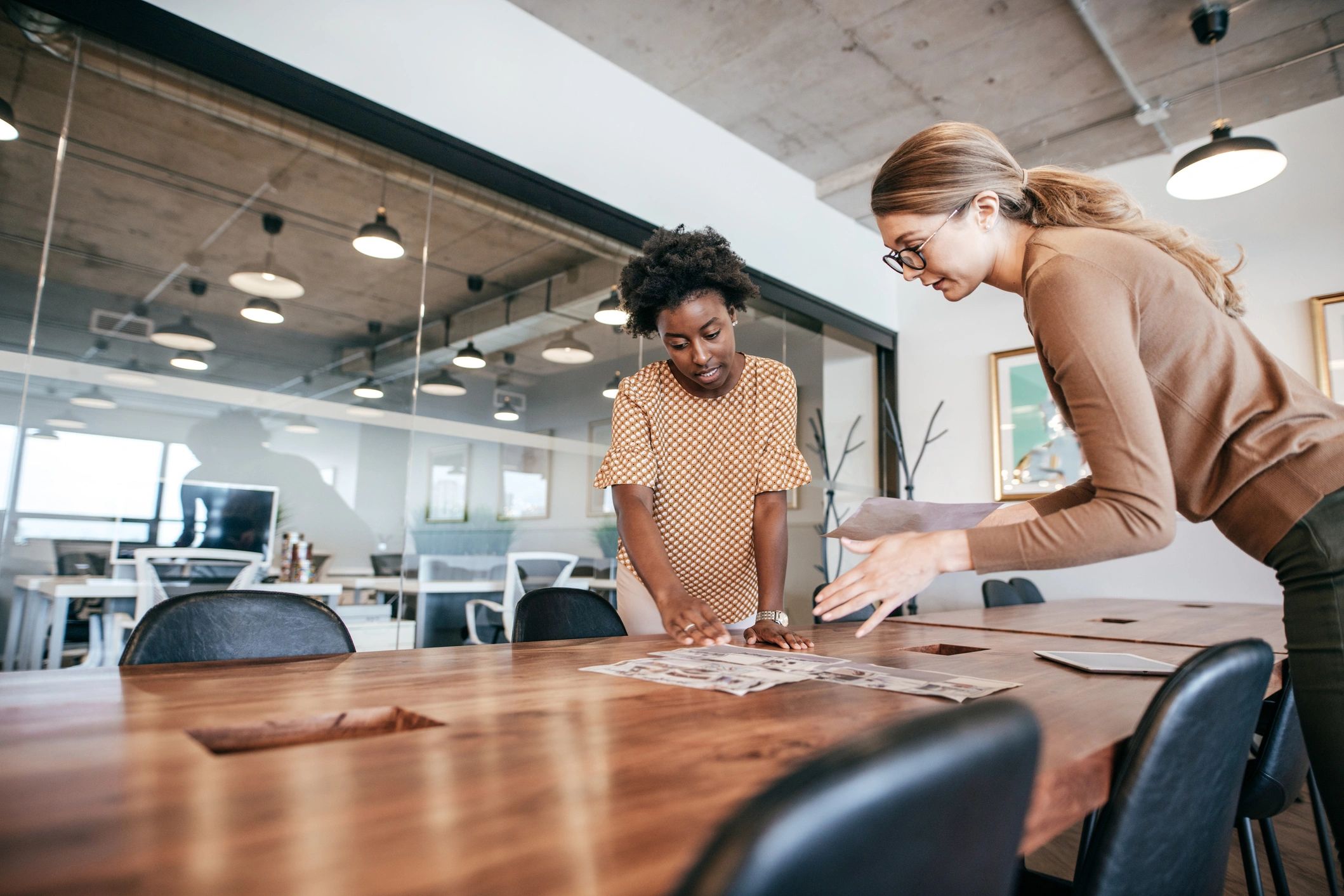Two women collaborating over papers on a wooden table.