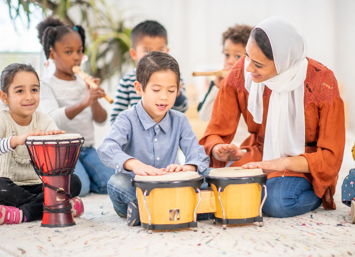 Children and a teacher playing drums and flutes in a music class.