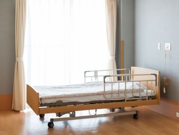 Empty hospital bed by a large window with curtains.