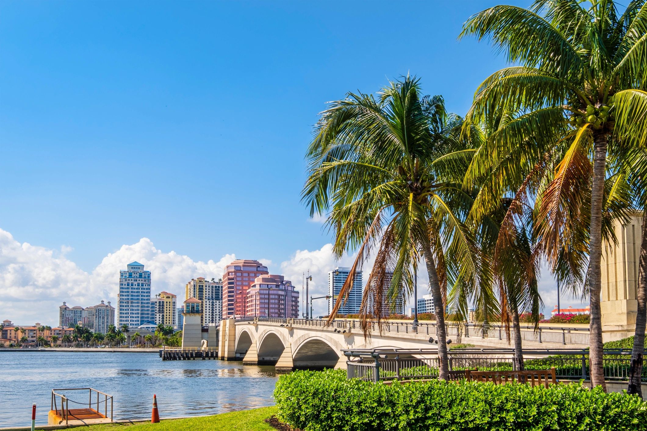 West Palm Beach skyline across the water, with palm trees and a bridge in the foreground.