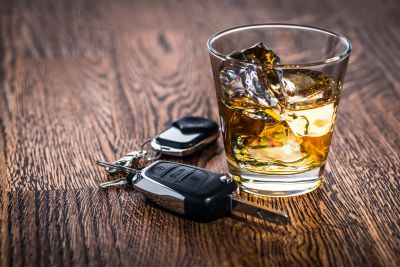 Car keys beside a glass of whiskey with ice on a wooden surface.