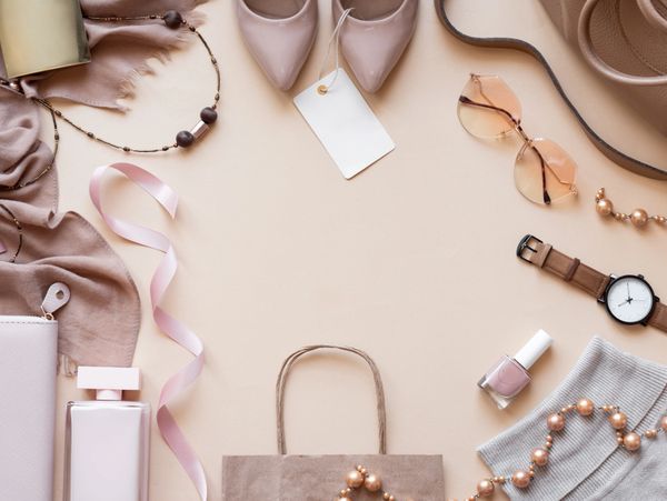 Flat lay of beige and pink fashion accessories and cosmetics on a neutral background.