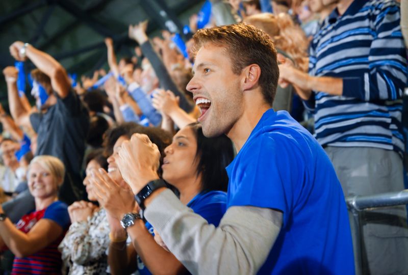 Cheerful fans celebrating while watching match in stadium.