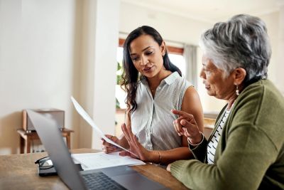 Two women discussing paperwork using a laptop.