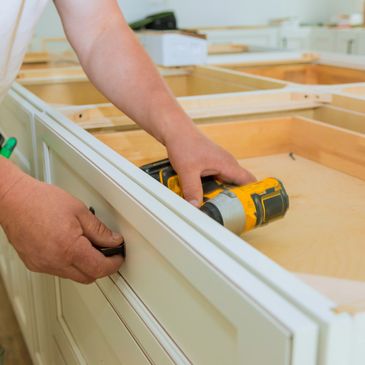 Person installing a cabinet handle with a power drill nearby.