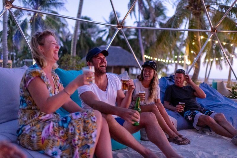 Friends laughing around the bonfire on the beach at sunset