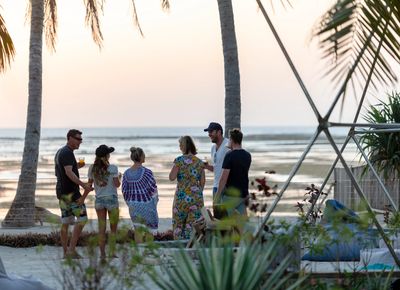 A group of people socializing near the beach at sunset.