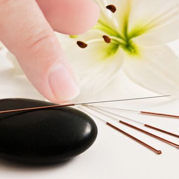 Finger touching acupuncture needle on black stone with white flower background.